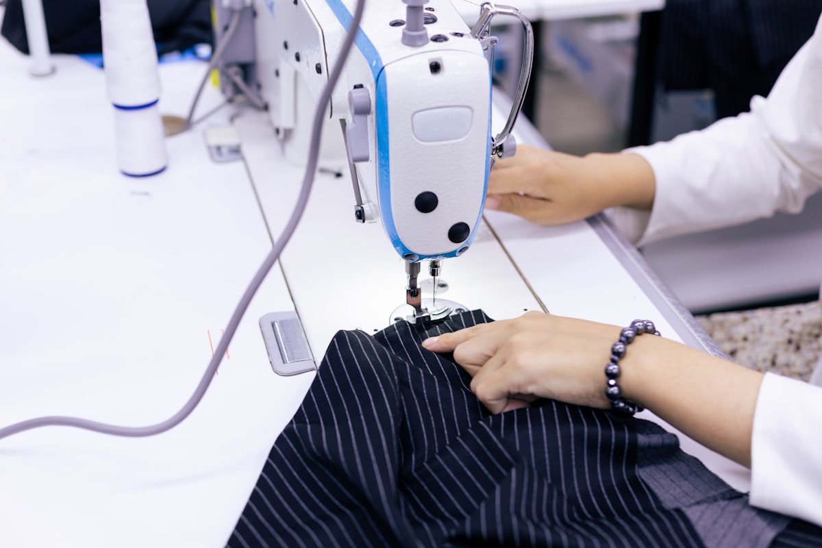 Hands guiding striped woven fabric under an industrial sewing machine